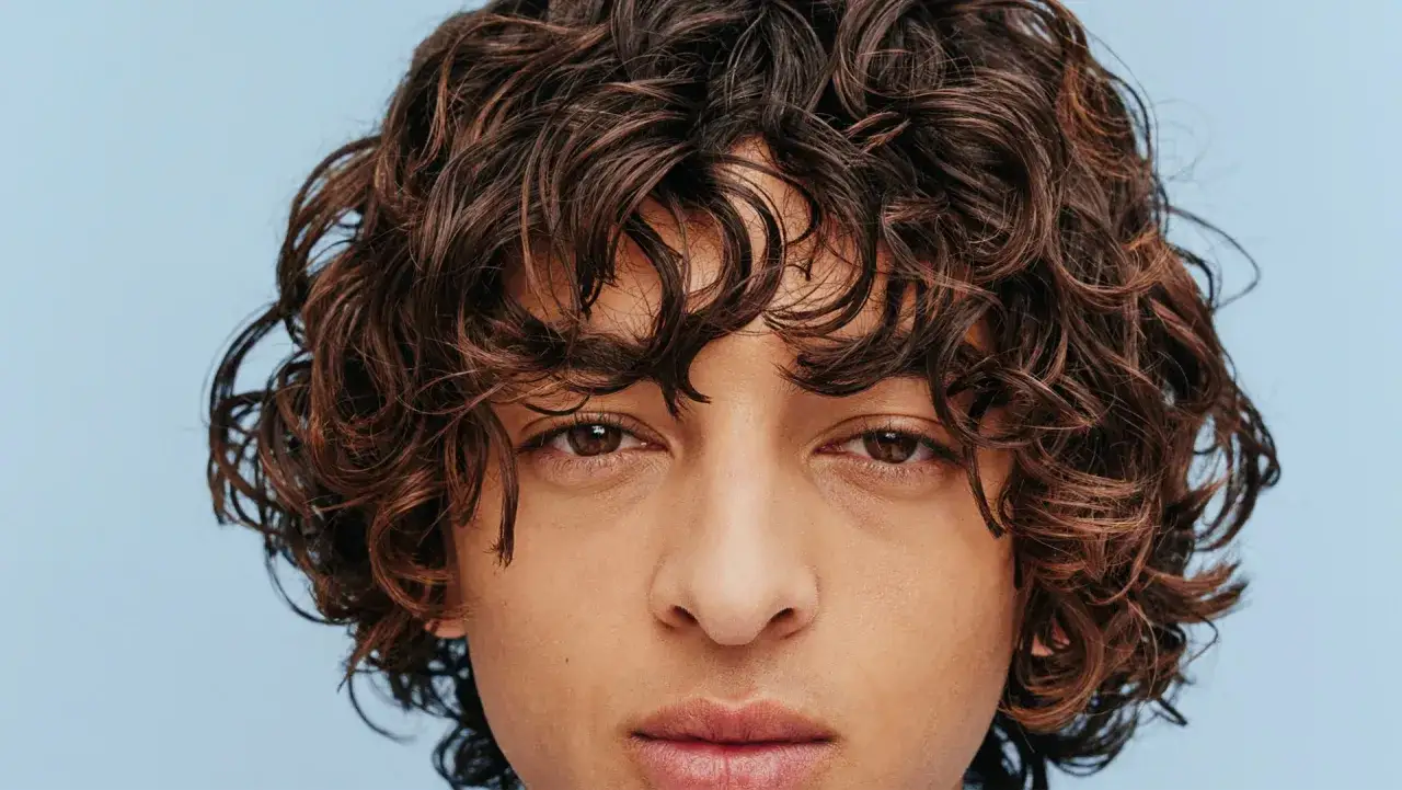 Gros plan sur le visage d'un homme aux magnifiques cheveux bouclés bruns. Ses boucles encadrent son visage, lui donnant un air décontracté et stylé.