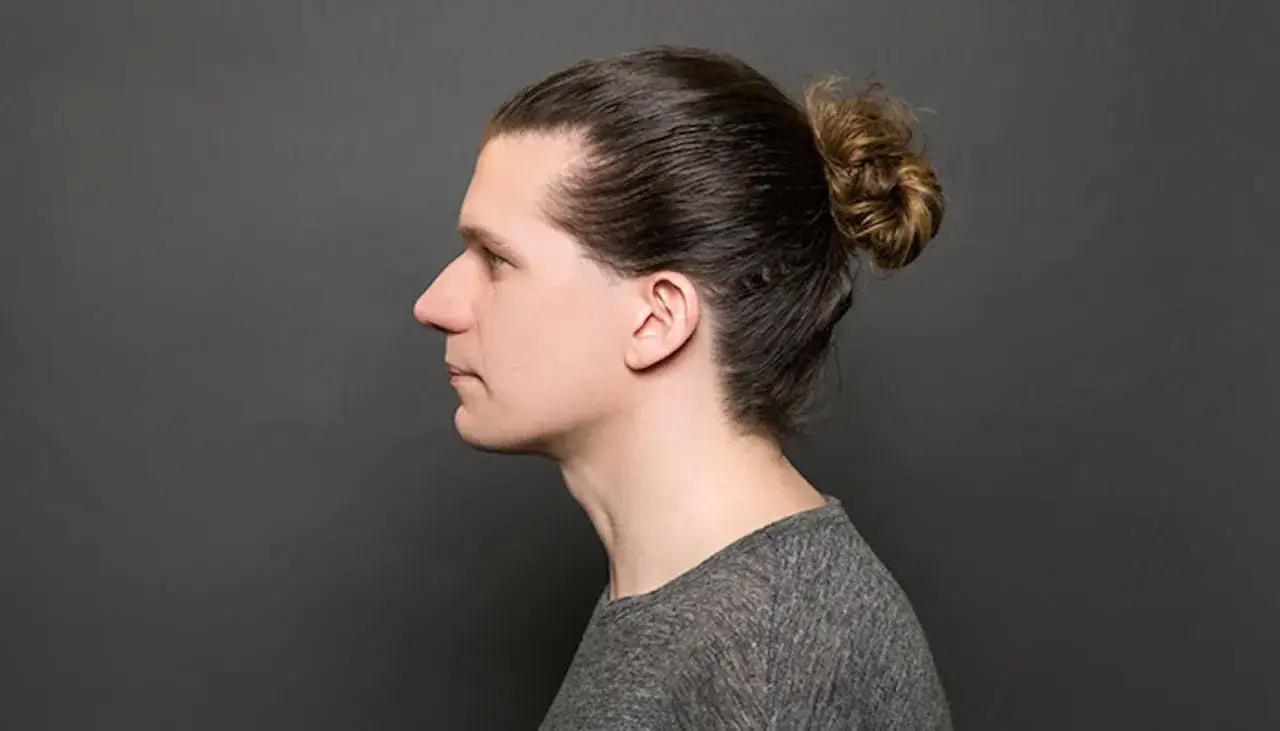 Profil d'un homme avec un man bun, cheveux bruns attach&eacute;s en chignon.