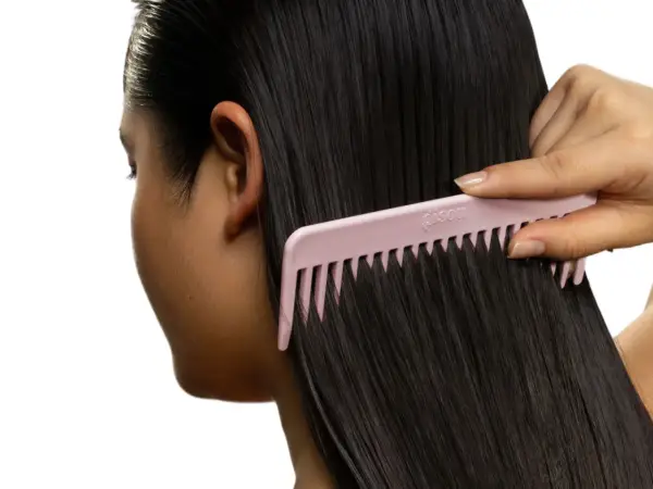 Une main peigne de longs cheveux noirs avec un peigne rose. Pas de nœud dans les cheveux, juste une chevelure soyeuse.