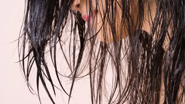 Cheveux sombres et humides tombant en cascade, révélant un aperçu d'une bouche rose et d'une peau claire.