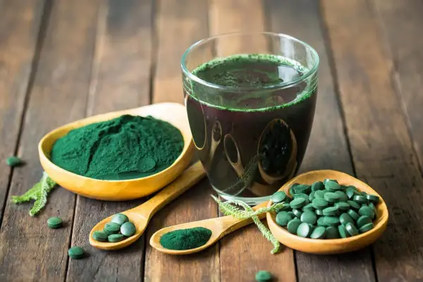 Spiruline en poudre, comprimés et boisson verte sur fond de bois. Découvrez les bienfaits spiruline cheveux pour une chevelure éclatante.
