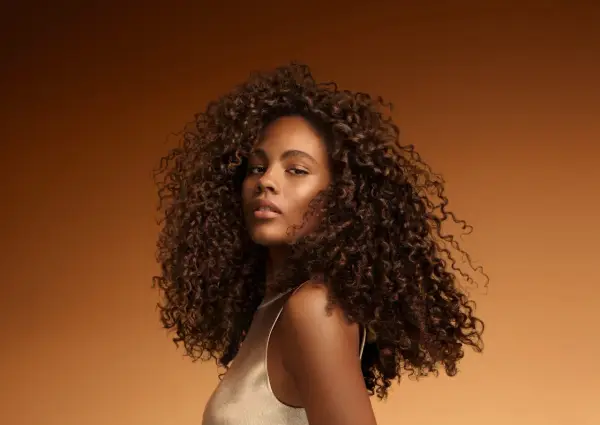 Une jeune femme aux cheveux bouclés et brillants, un exemple de comment bien rincer ses cheveux pour un éclat naturel.