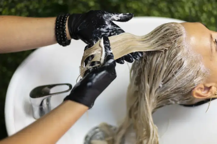 Application d'une patine sur des cheveux blonds. Le coiffeur, portant des gants noirs, applique le produit. Le temps de pose est crucial pour le résultat.