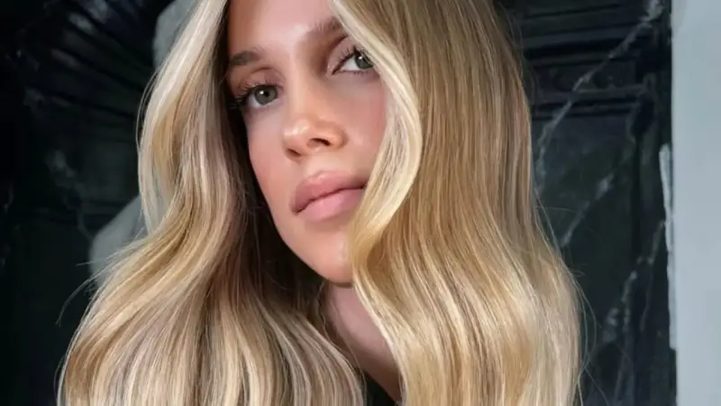 Une femme aux yeux verts et aux lèvres pulpeuses arbore une chevelure ondulée d'une magnifique teinte de blond.