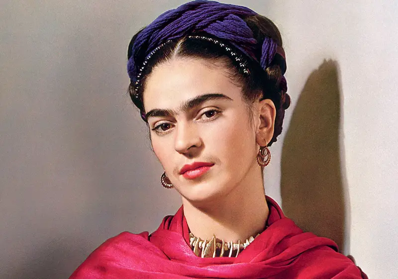 Portrait de Frida Kahlo avec sa célèbre coiffure torsadée violette, un foulard rouge vif et des bijoux ethniques.